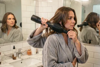 Femme utilisant une brosse soufflante pour coiffer ses cheveux devant un miroir de salle de bain